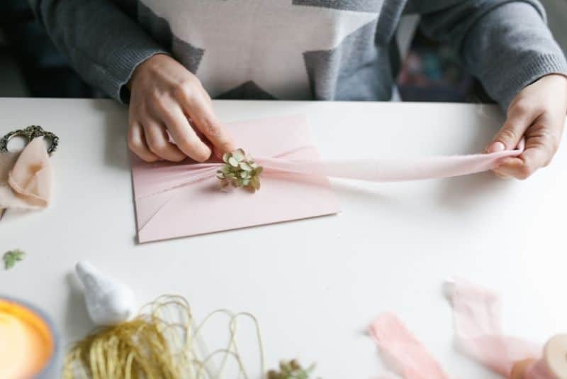female tying ribbon around diy wedding invitation