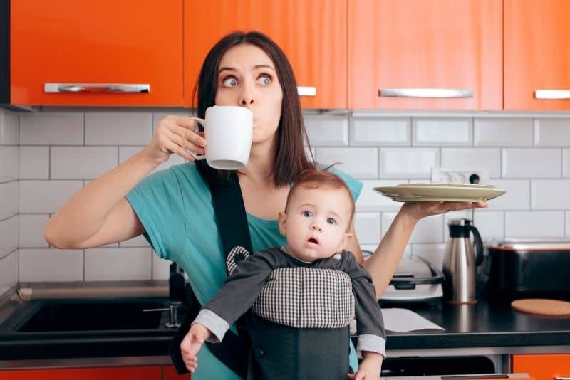Mom drinking coffee with child strapped to her body.
