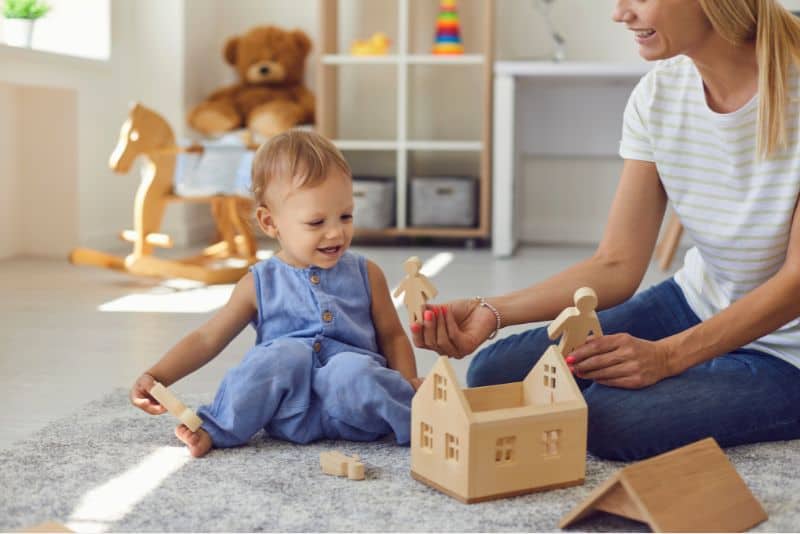 Smiling young mixed race woman babysitter enjoying playing with little adorable funny baby