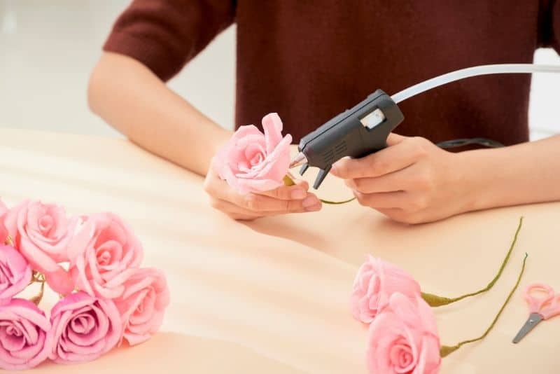 woman using hot glue gun to make pink paper roses